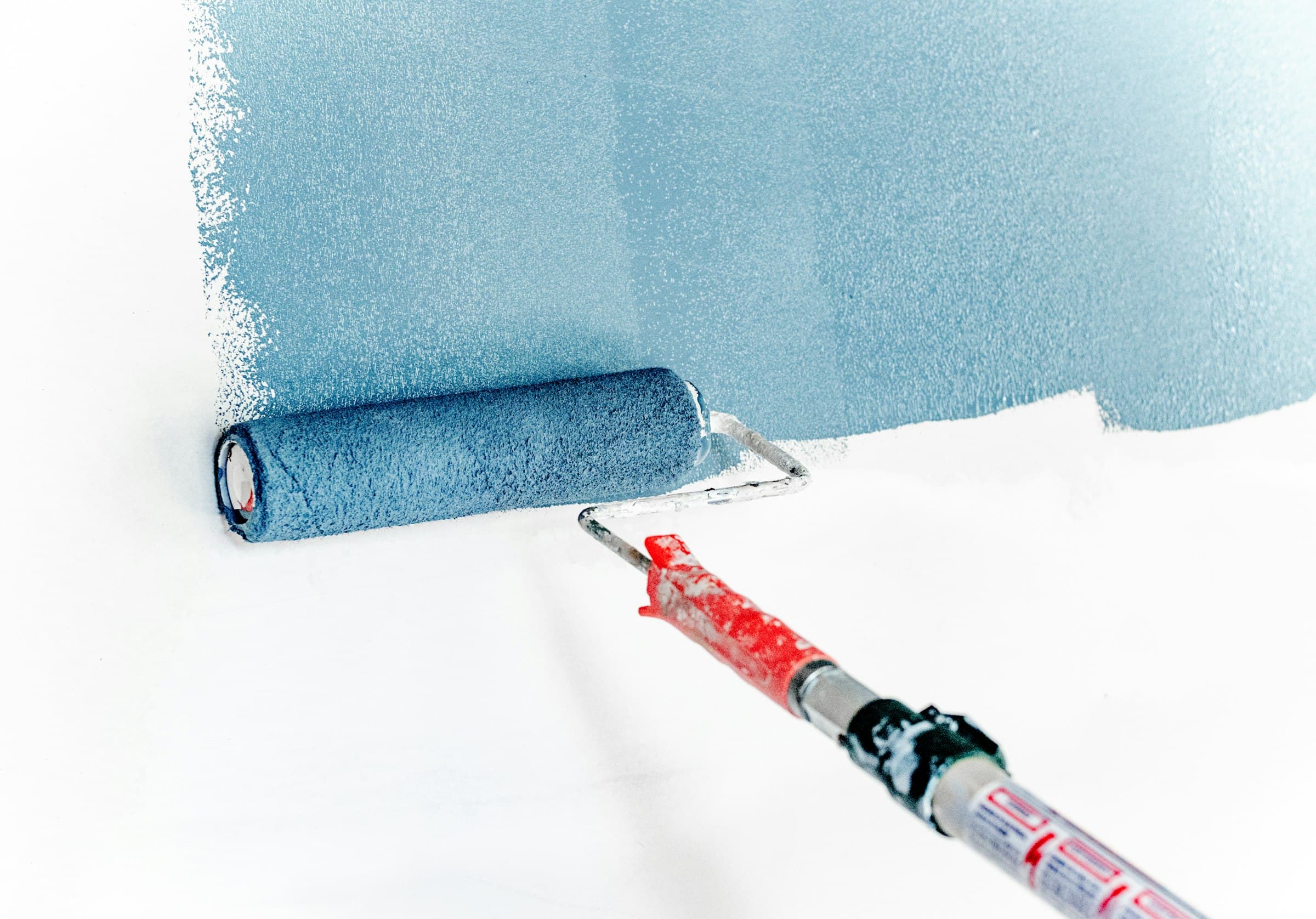 Farbrolle trägt taubenblaue Wandfarbe gleichmäßig auf eine weiße Wand auf